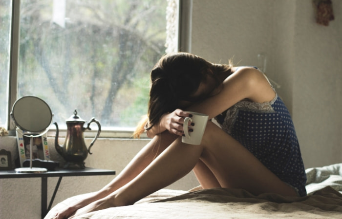 woman with her face buried in her knees on bed