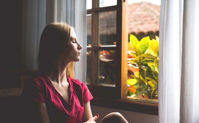 woman sitting by an open window with eyes closed