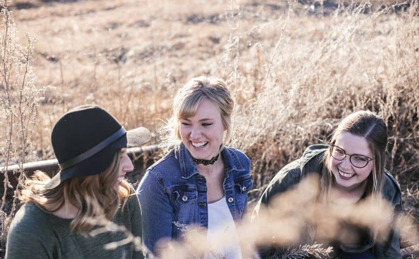 a group of women laughing together in a grass field