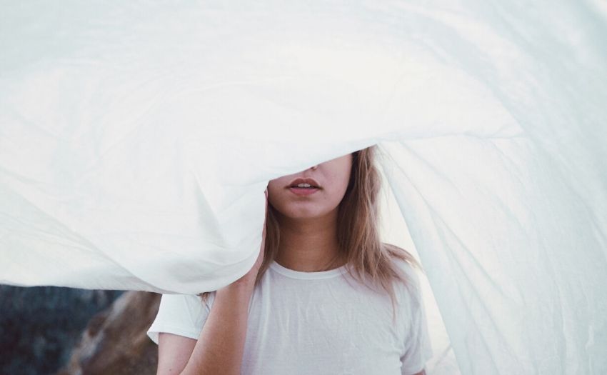 woman hiding her face behind a white sheet