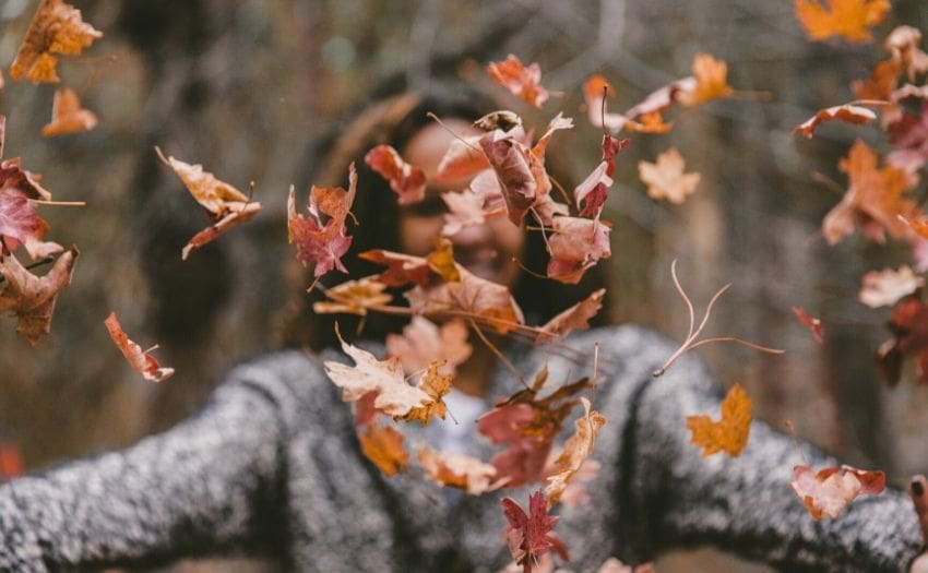 woman tossing autumn leaves