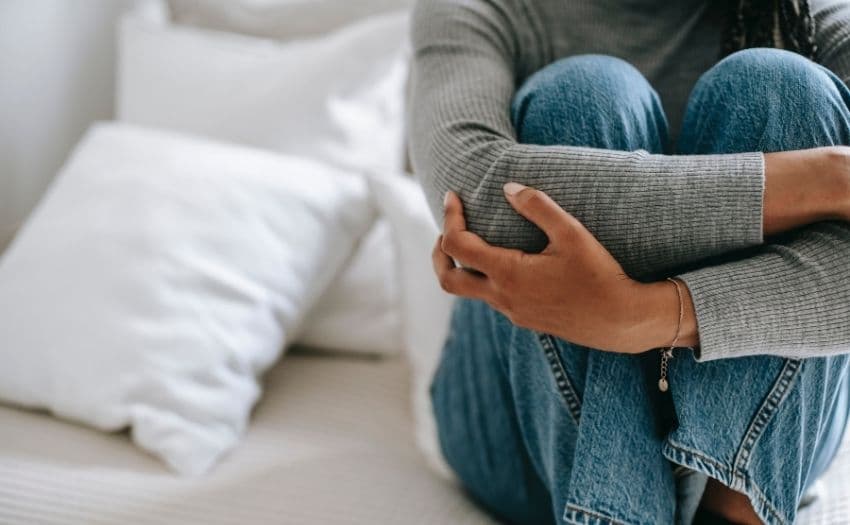 woman hugging her legs on the bed